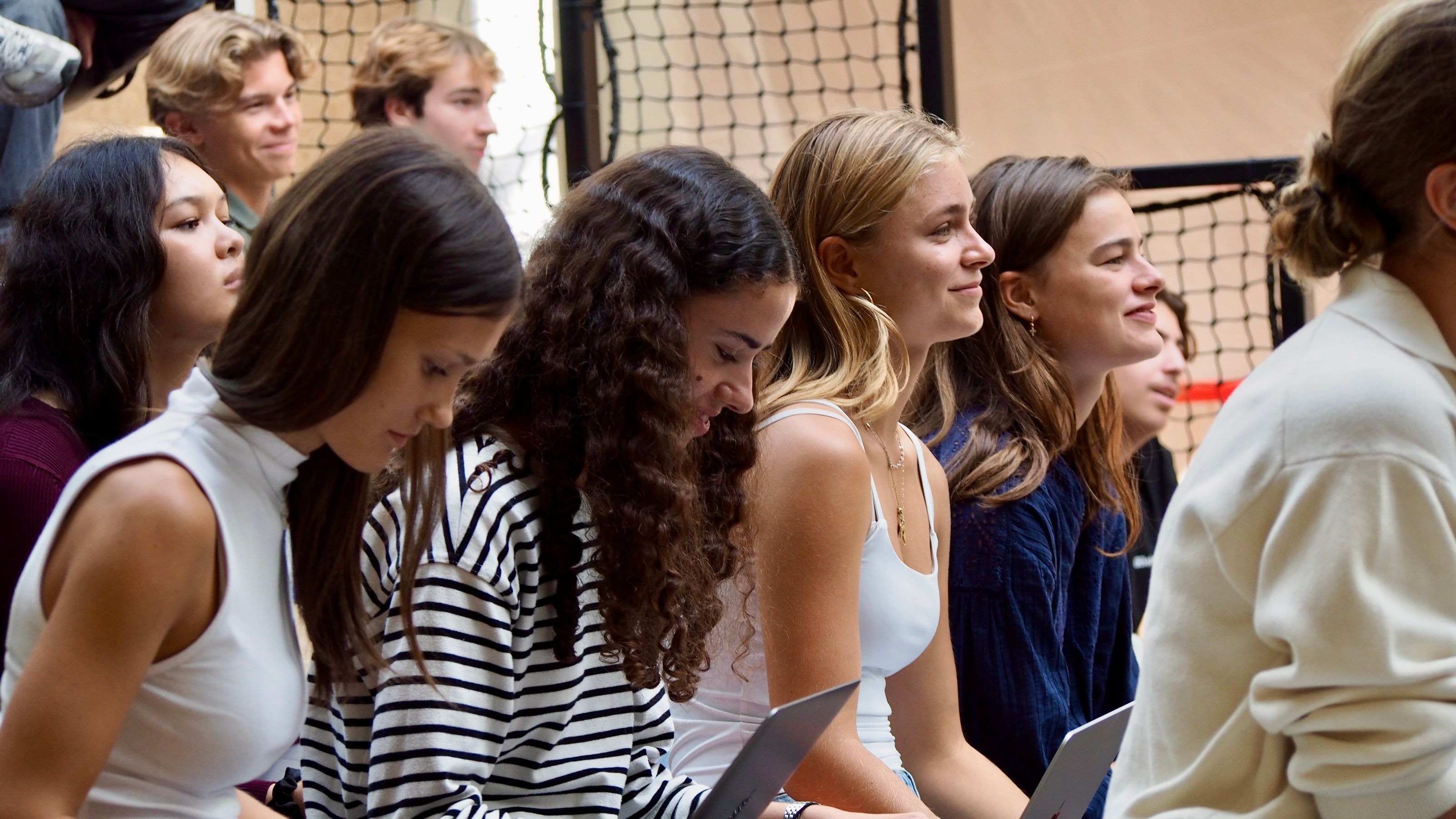 Group of young people sitting closely together indoors, some smiling and holding laptops.