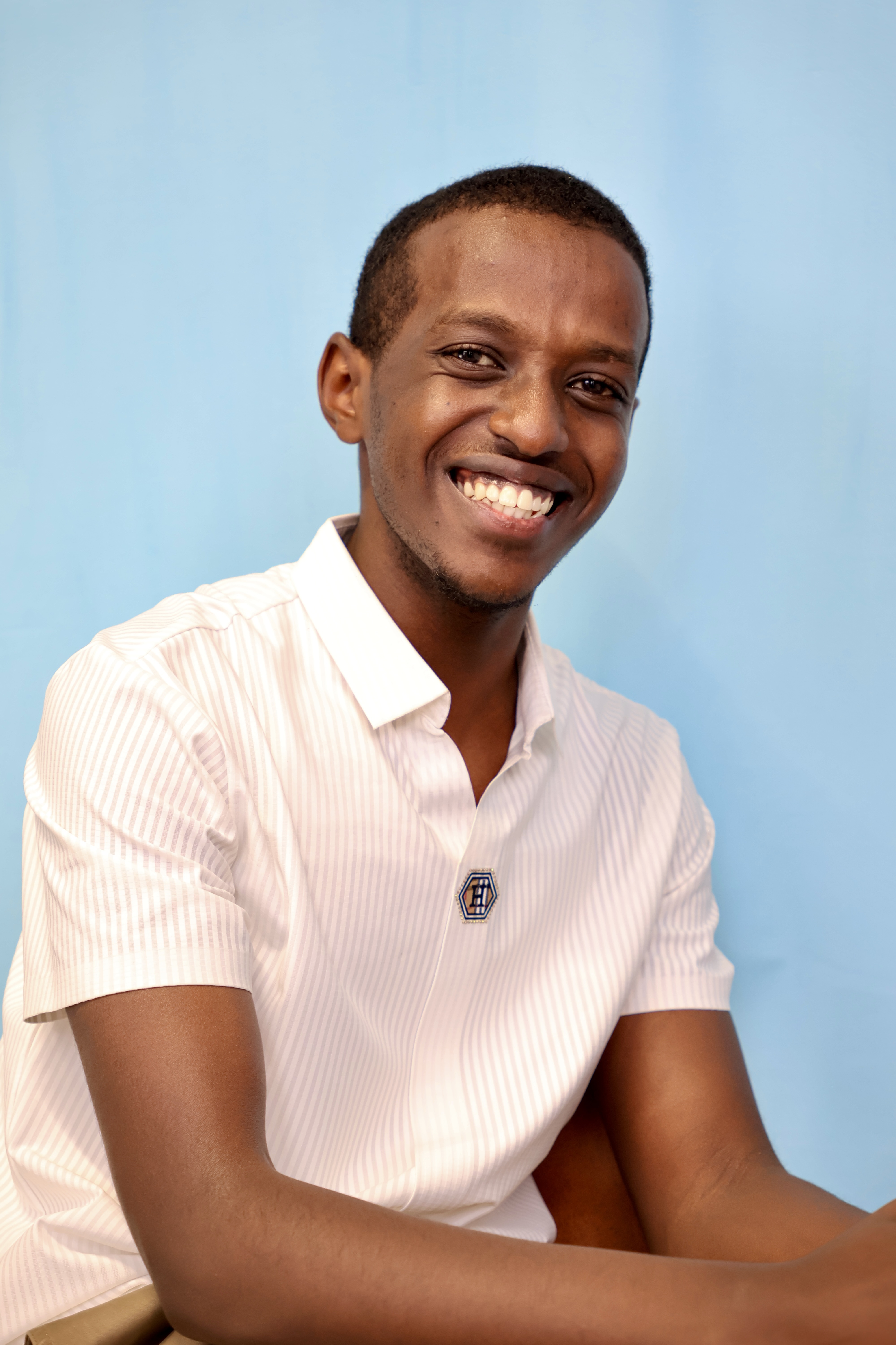 Smiling young man wearing a white short-sleeve shirt sitting in front of a blue background.