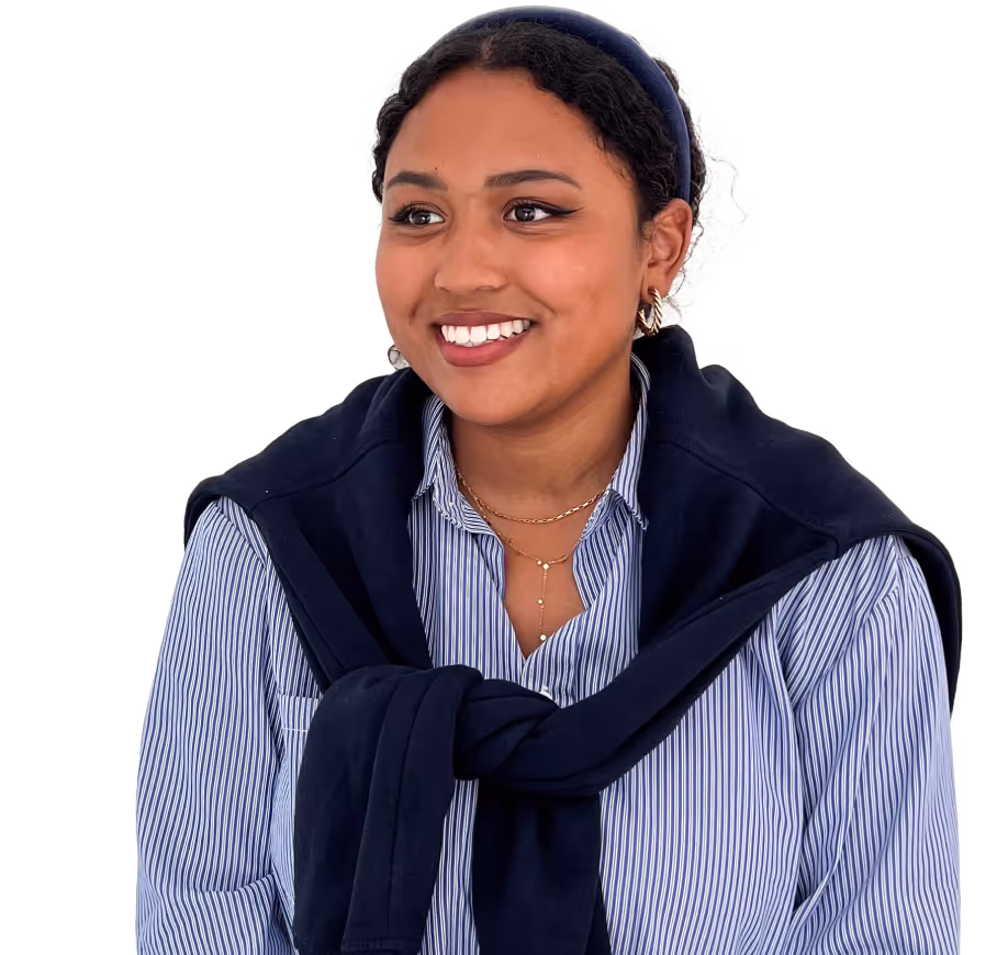 Smiling young woman with dark curly hair wearing a striped shirt and a navy sweater tied around her shoulders.