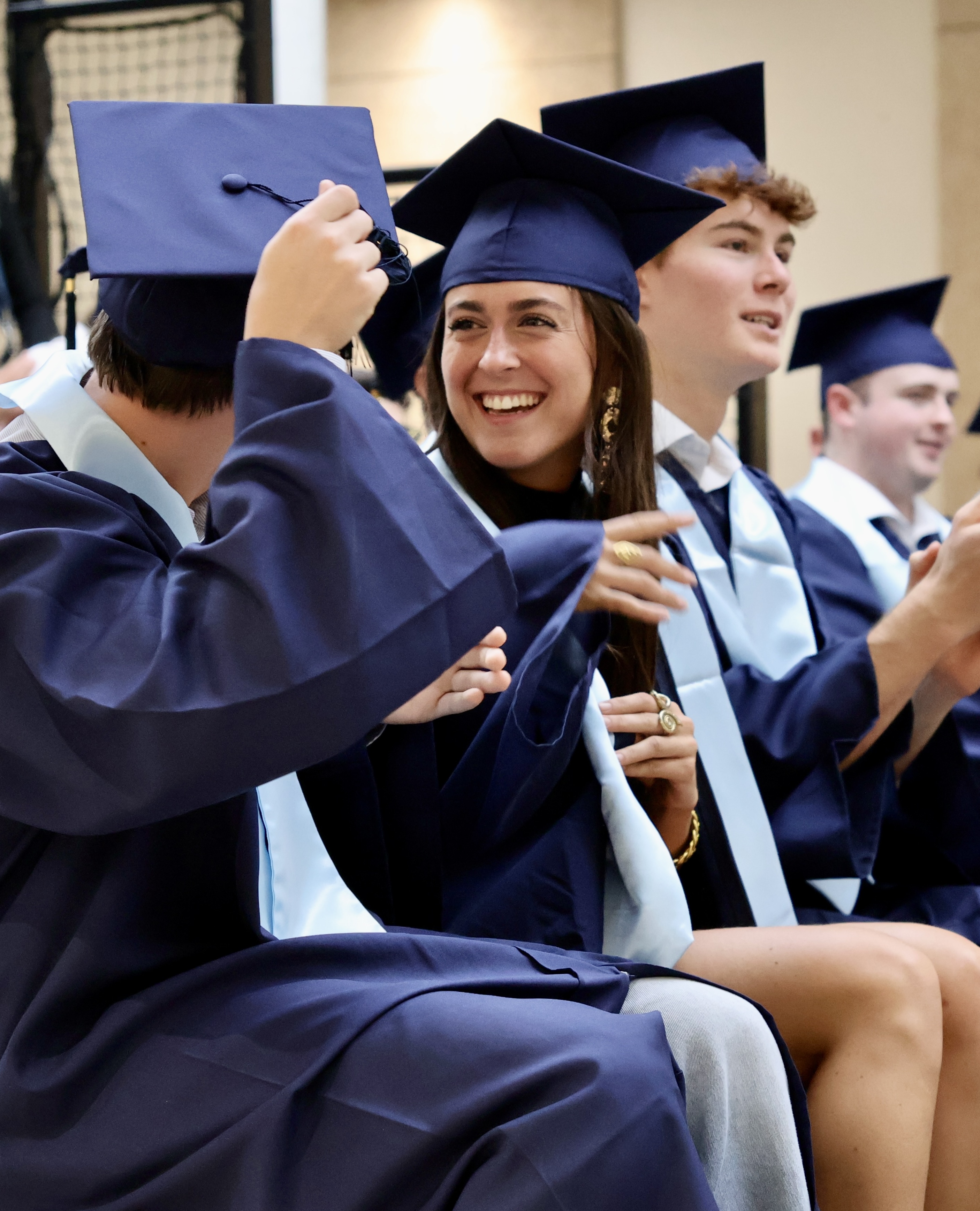 Smiling graduates in navy caps and gowns sitting together indoors, celebrating their achievement.