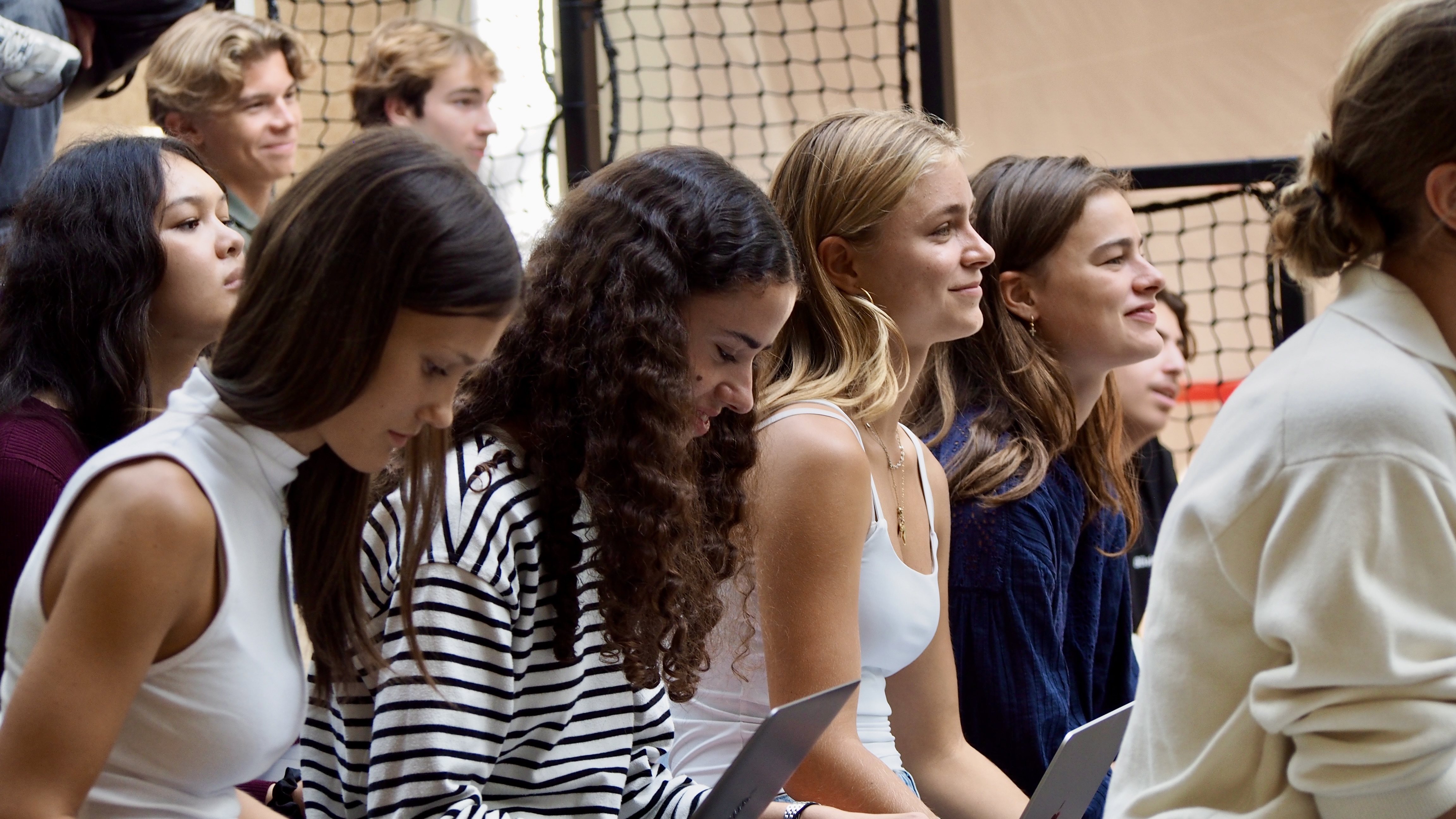Group of young people sitting closely together indoors, some smiling and holding laptops.