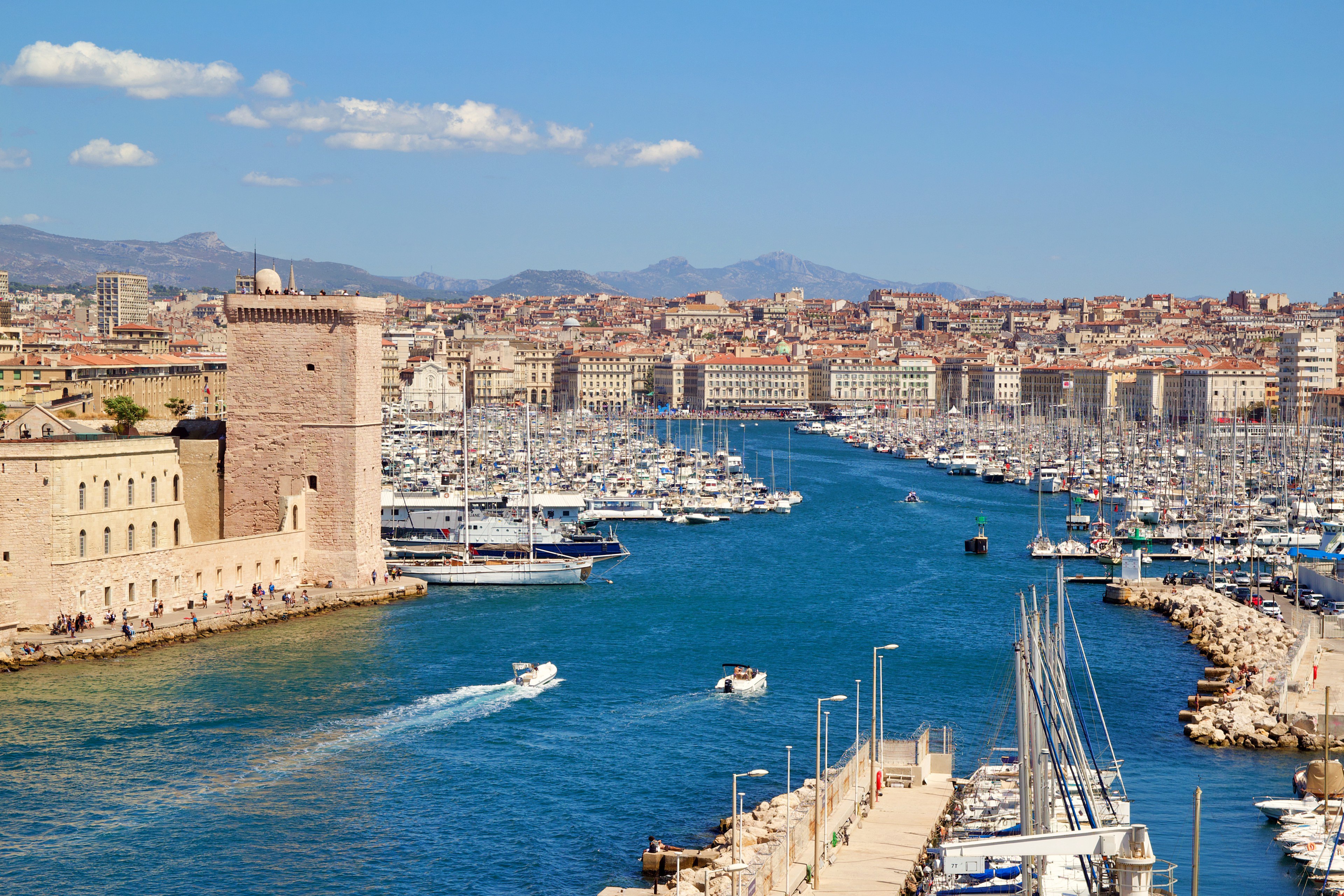 Marseille harbor with many docked sailboats, historic stone buildings, and blue water under a clear sky.