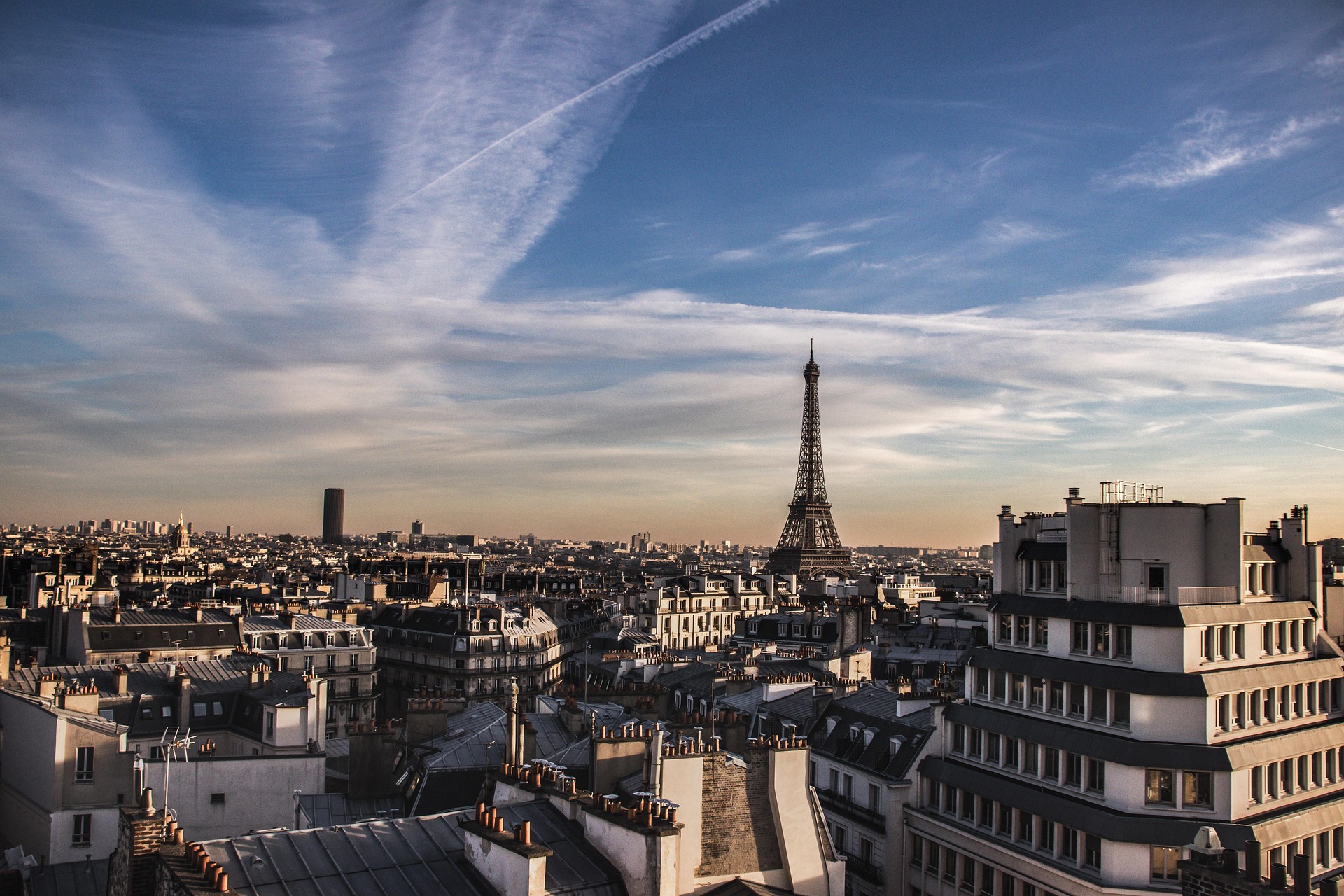 View of Paris rooftops with the Eiffel Tower under a partly cloudy blue sky.