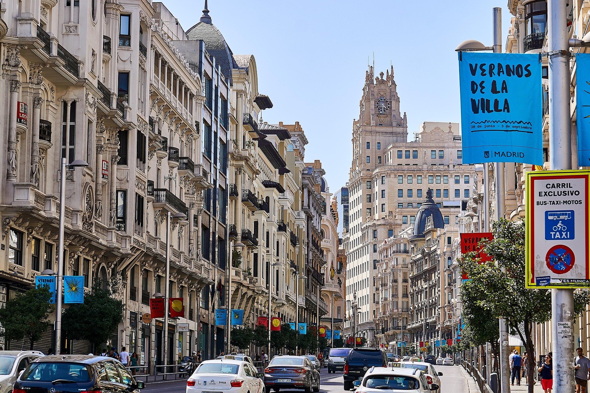 Busy street in Madrid with historic buildings, cars, and banners reading 'Veranos de la Villa'.