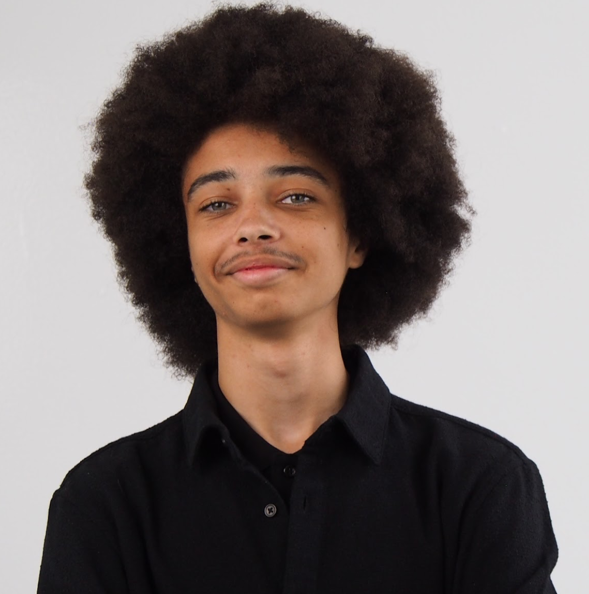 Young man with a large curly afro wearing a black button-up shirt against a light gray background.